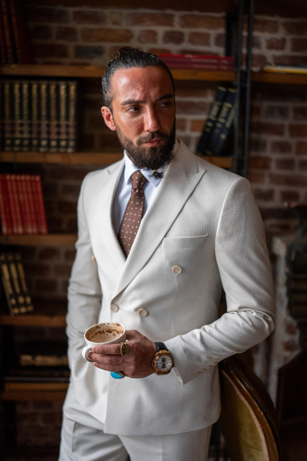 Elegant off-white double-breasted suit for men by Mazonni, styled with a brown tie and dress shirt in a vintage library setting