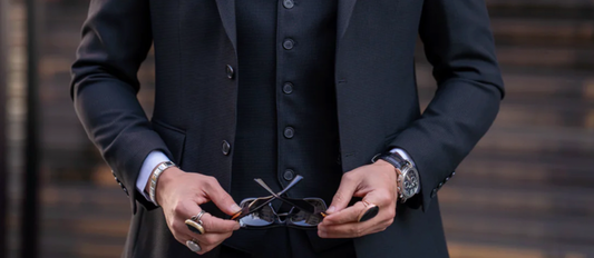 Close-up of man in dark three-piece suit holding eyeglasses — essential men’s formalwear for events and special occasions