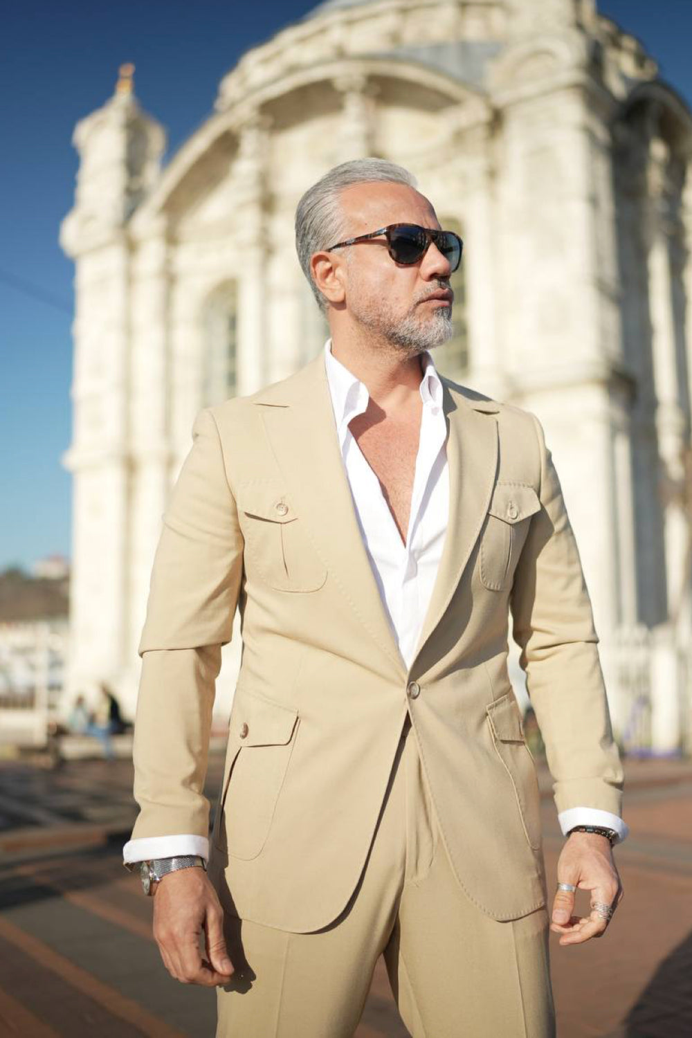 Men's beige fashion suit by Mazonni, featuring utility-style pocket design and casual elegance near historic architecture