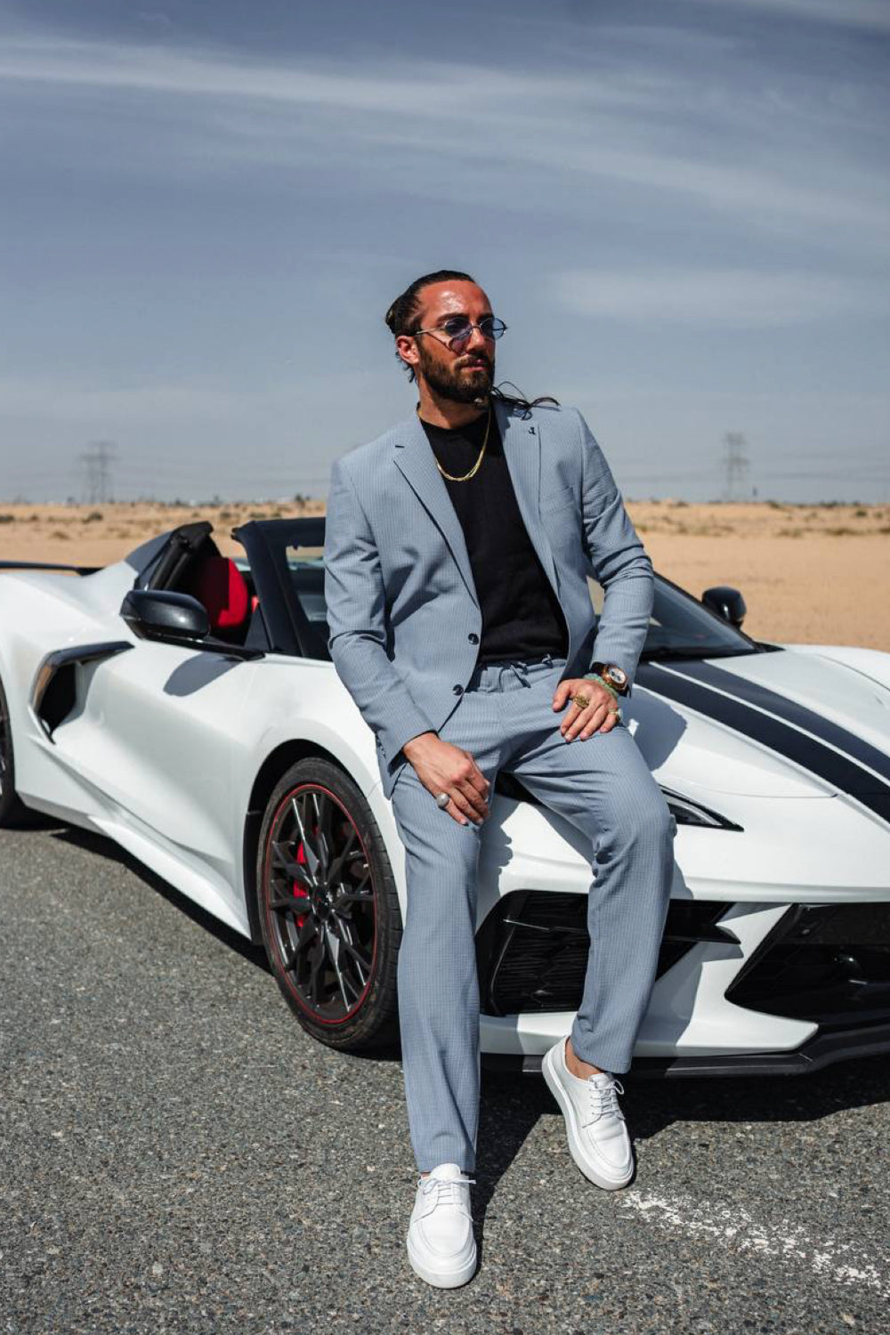 Light blue Mazonni men's suit paired with black shirt and white sneakers, styled against a luxury sports car for a modern streetwear twist