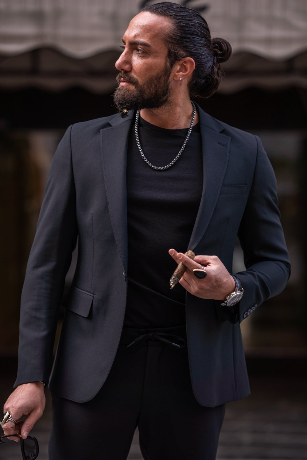 Close-up of Mazonni black blazer worn with round sunglasses and chain necklace for contemporary menswear