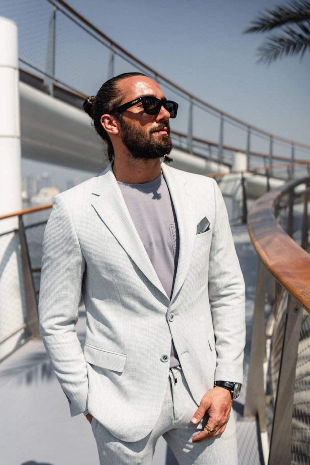 Slim-fit men's suit in light grey by Mazonni, worn casually with sneakers and shades for an effortless modern look