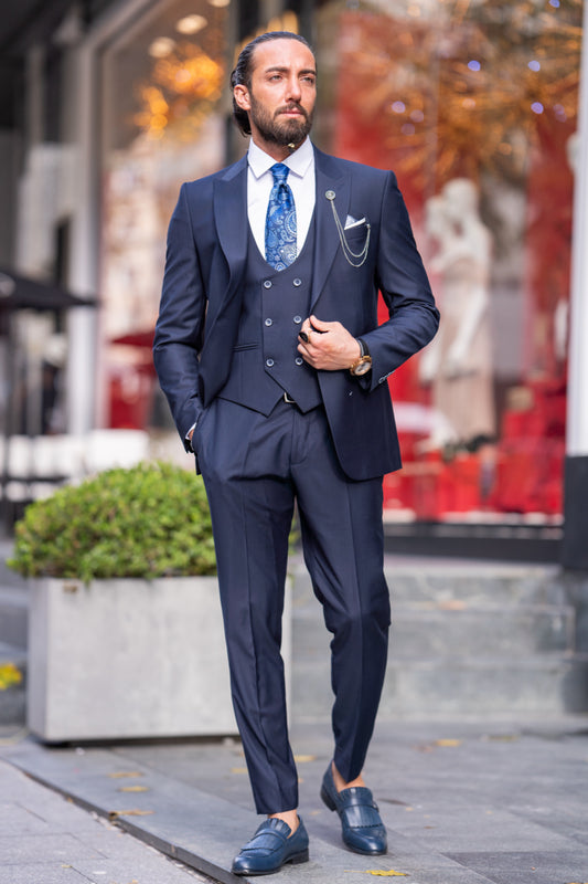 Navy blue three-piece men's suit by Mazonni with patterned tie and chain detail, perfect for formal events