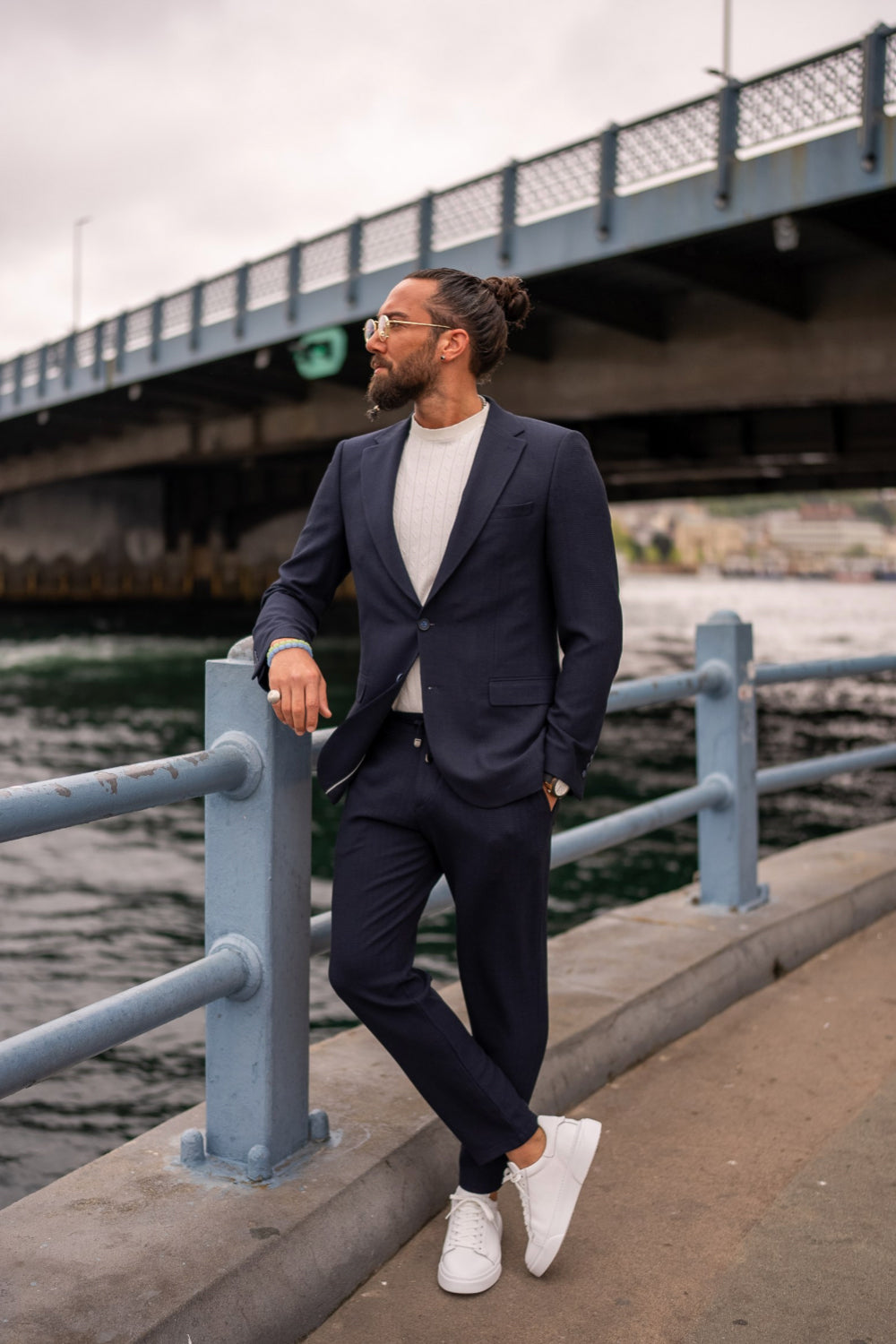 Stylish navy suit for men by Mazonni paired with minimalist sneakers, showcasing relaxed business casual fashion on a waterfront promenade